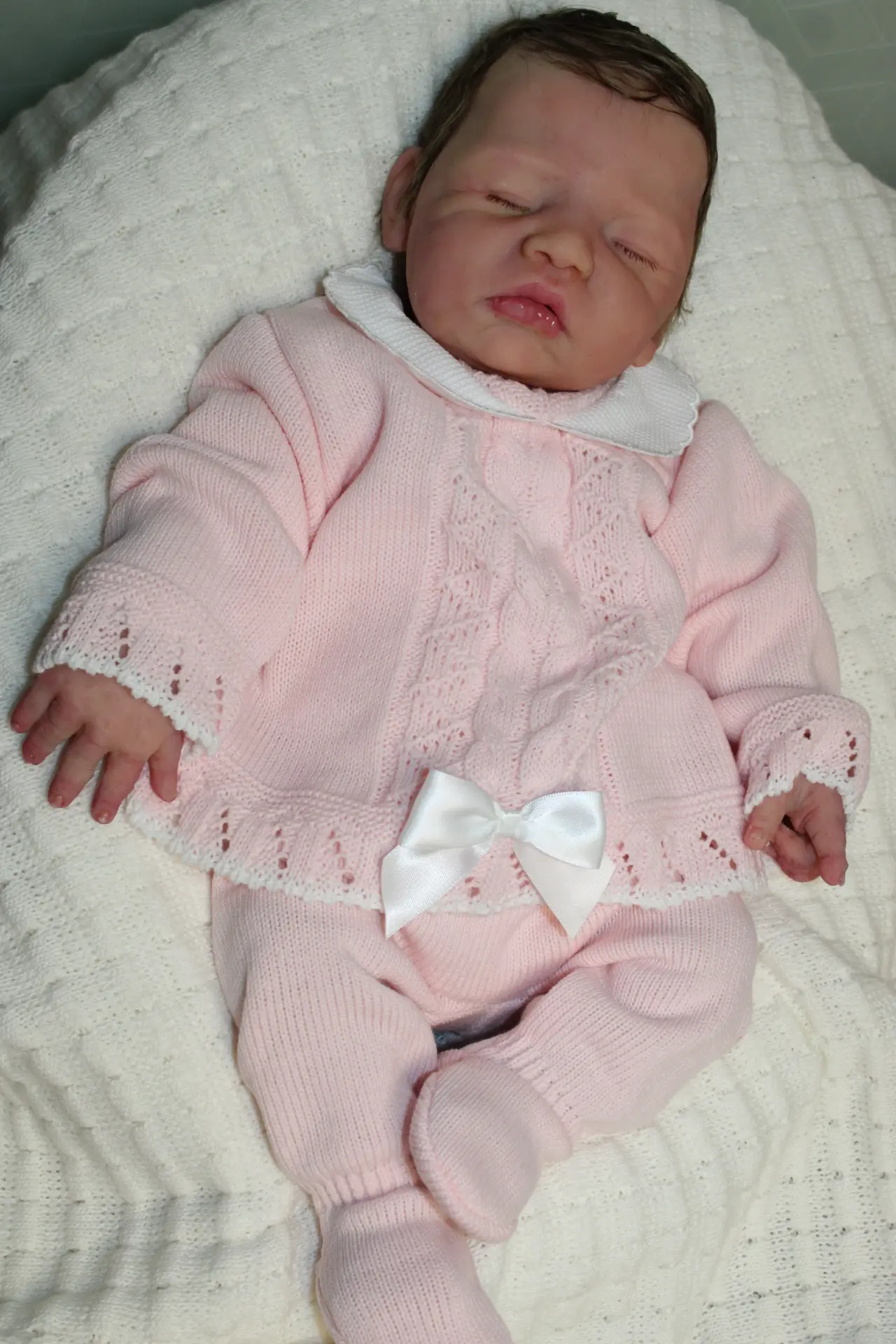 Bébé reborn allongé sur le dos dans une tunique rose avec un ruban blanc.