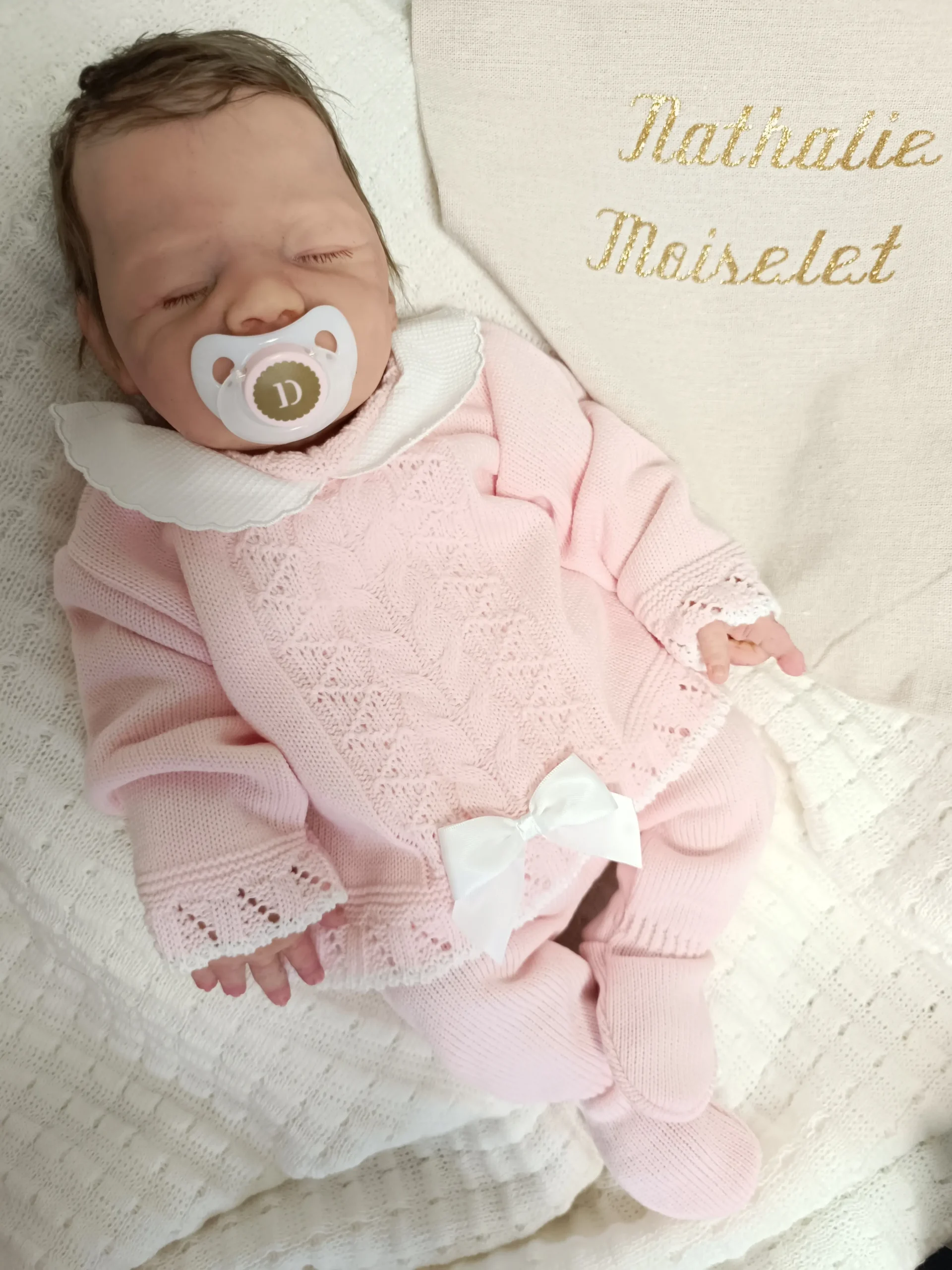 Photo d'un bébé Reborn en silicone allongé dans une tunique pour dormir avec une tututte.